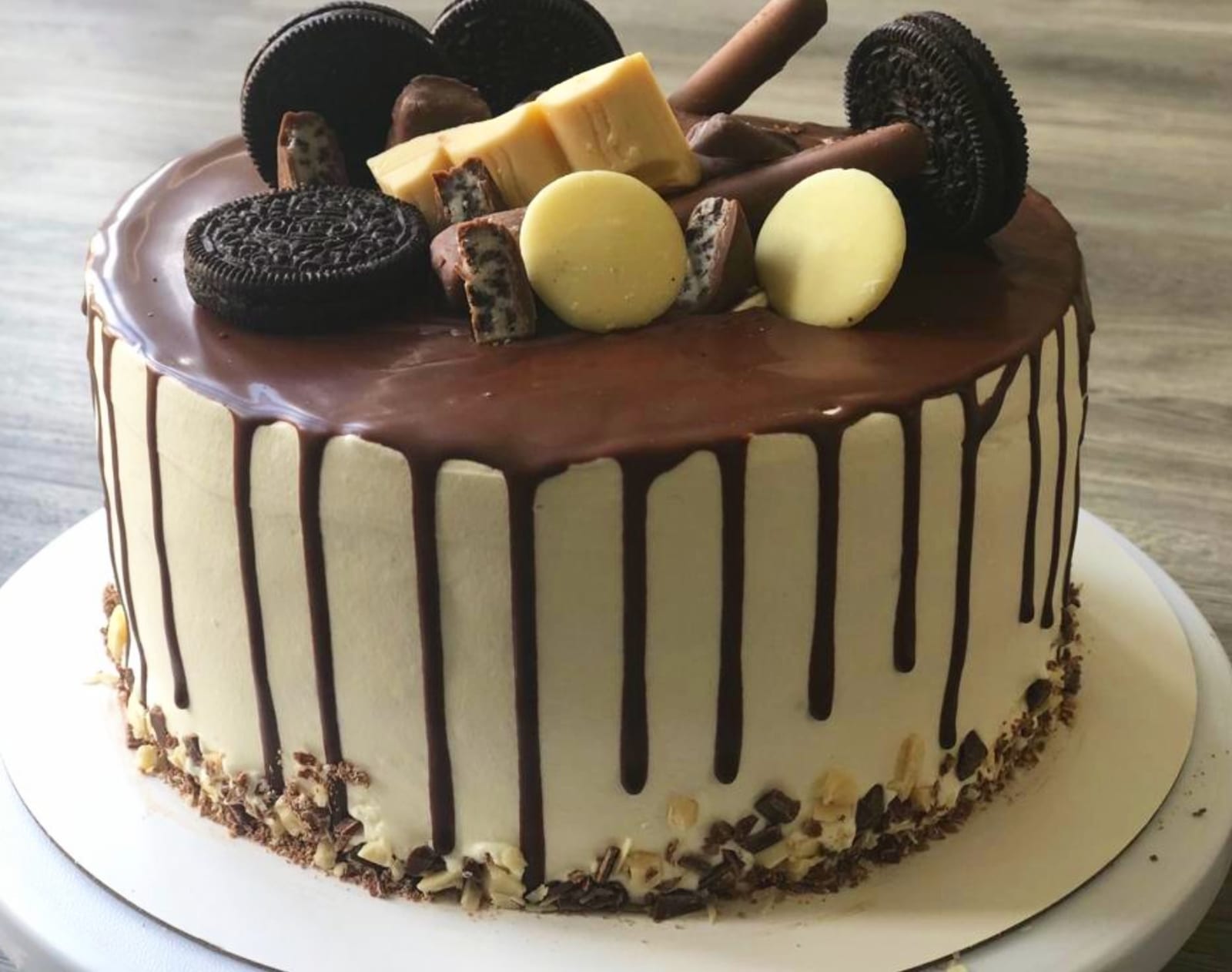 Cake with a chocolate drip over pale buttercream, topped with Oreos and white and dark chocolate pieces, with chocolate chips pressed around the base.